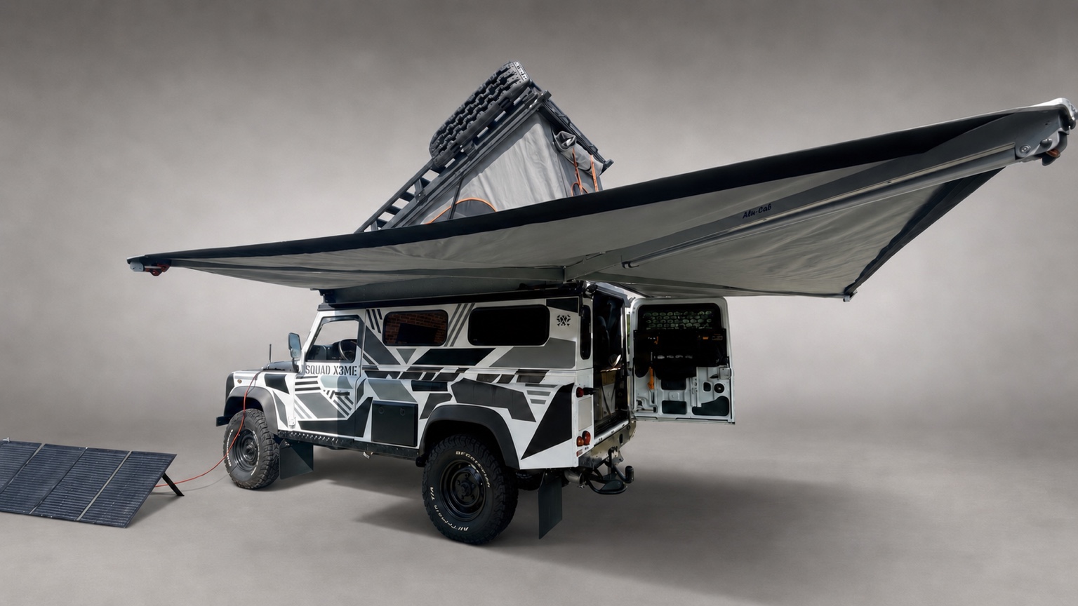 Der Defender im Camp-Aufbau mit geöffnetem Aufstelldach, weit ausladender Markise, offener Hecktür und mobilem Solarmodul.