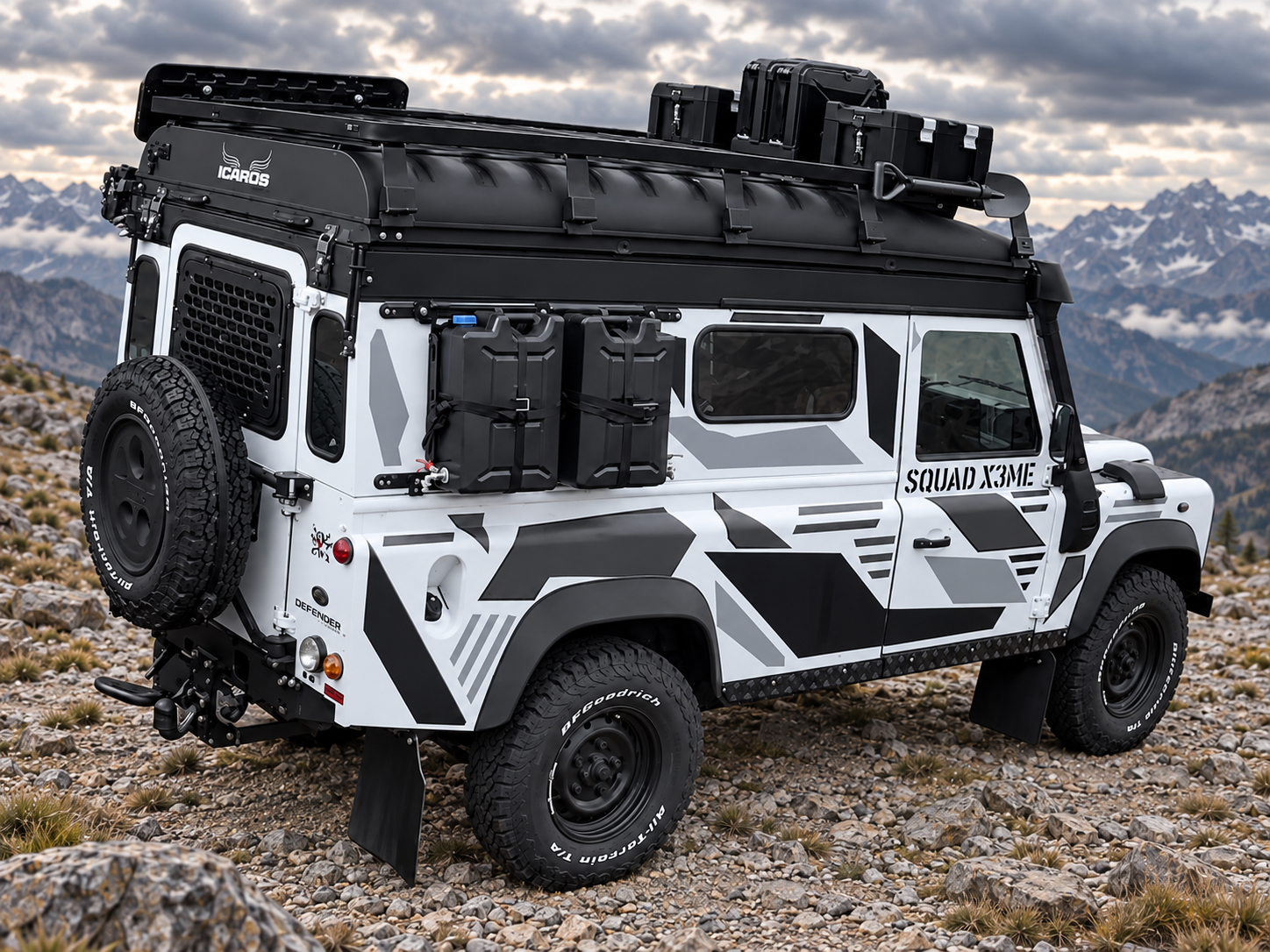 Der Land Rover Defender von schräg hinten mit Ersatzrad, seitlichen Kanistern, Dachausrüstung und grauweißem X3ME-Design in digital ergänzter Felslandschaft.